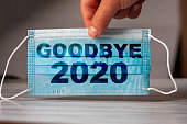 hand holds a medical and protective mask with the word GOODBYE 2020. Concept of coronavirus quarantine. Prevent or stop the spread of the COVID-19 worldwide.