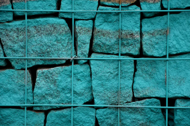 stone gabion wall sprayed with street vandal, vandalism. Street art. turquoise silver and purple overlap granite cubes lined up behind the mesh of the basket. retaining wall, texture, background stone, gabion, wall, sprayed, with, street, vandal, vandalism, turquoise, silver, paint, painting, purple, overlap, granite, cubes, lined, behind, mesh, basket, retaining, wall, texture, background, puzzle, dirty, cleaning, tag, steel, wire, wired, urban, purple graffiti metallic wall stock pictures, royalty-free photos & images