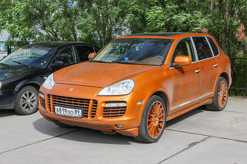 Novyy Urengoy, Russia - June 27, 2020: Orange crossover Porsche 957 Cayenne in the city street.