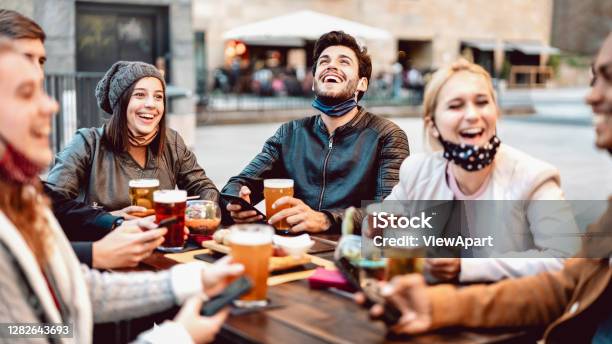 Young Friends Drinking Beer Wearing Face Mask New Normal Lifestyle Concept With People Having Fun Together Talking On Happy Hour At Outside Brewery Bar Bright Warm Filter With Focus On Central Guy Stock Photo - Download Image Now