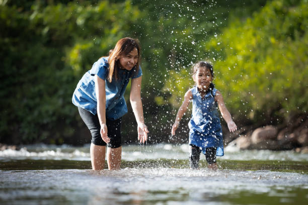 asiática madre y su niña jugando en el río junto con la diversión y disfrutar con la naturaleza. - park child asia lifestyles fotografías e imágenes de stock