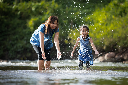 Asian mother and her child girl playing in the river together with fun and enjoy with nature.