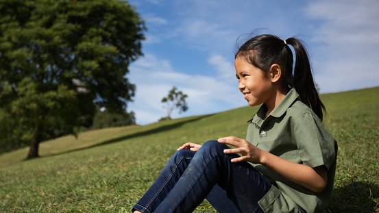 Asian child girl sitting on the hill with green grass to enjoy with beautiful nature in the summer time.