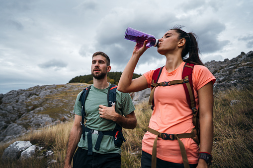Young woman drinking water while her partner standing next to her during hiking adventure.