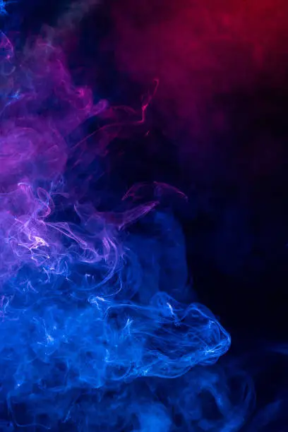 Photo of Conceptual image of colorful red and blue color smoke on dark black background.