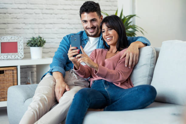 istock Happy young couple making a video call with smart phone while sitting on couch at home. 1282650159