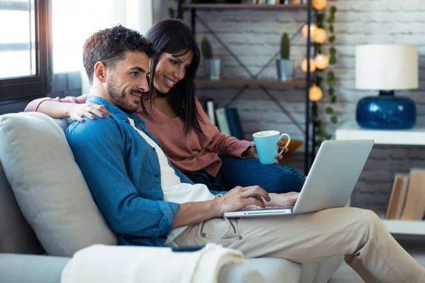 istock Happy beautiful couple using computer while sitting on the couch at home. 1282650292