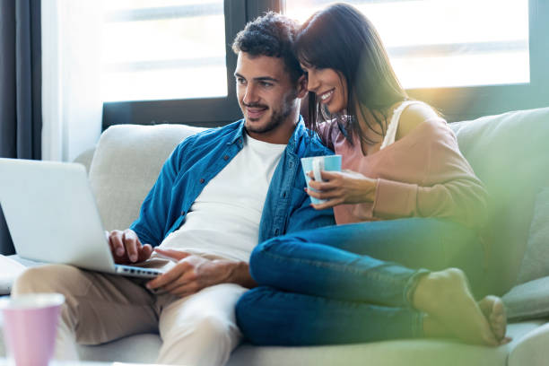 Happy beautiful couple using computer while sitting on the couch at home.
