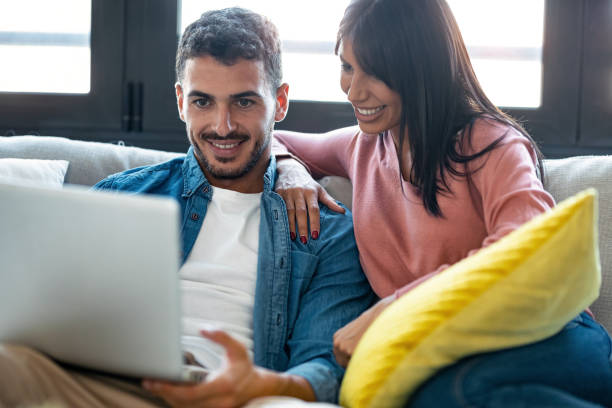 istock Happy beautiful couple using computer while sitting on the couch at home. 1282650796
