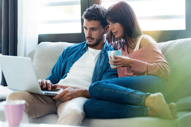 istock Confident beautiful couple using computer while sitting on the couch at home. 1282651504