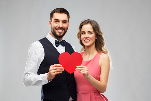 valentines day, love and people concept - happy couple in party clothes with red heart over grey background