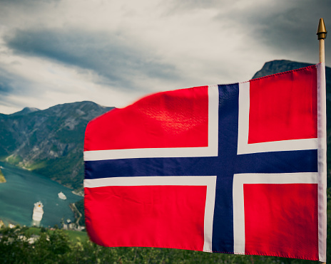 Norwegian flag and beautiful view over Geirangerfjorden from Flydalsjuvet viewing point. Tourist attraction. Tourism vacation and travel.