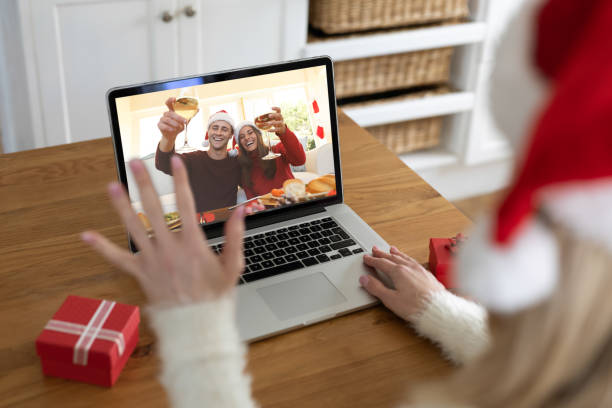 vista posteriore della donna con cappello di babbo natale che saluta mentre fa una videochiamata con la coppia in cappelli di babbo natale che brindano o - santa claus waving christmas photography foto e immagini stock