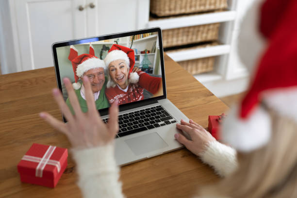 vista posteriore della donna con cappello di babbo natale che saluta mentre fa una videochiamata con una coppia senior in cappelli di babbo natale - santa claus waving christmas photography foto e immagini stock