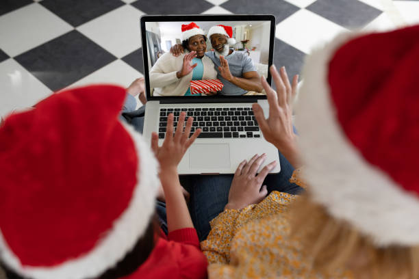 vista trasera de la mujer y la hija en sombreros de santa saludando mientras tiene un videollamada con la pareja de la tercera edad en - santa claus waving christmas photography fotografías e imágenes de stock