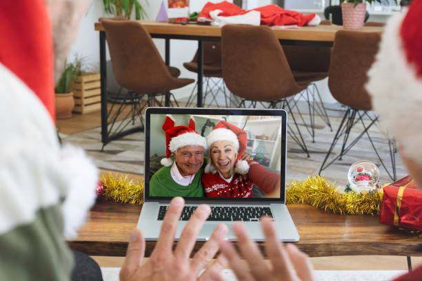 vista trasera del hombre y el hijo en sombreros de santa saludando mientras tiene un videocall con la pareja mayor en santa h - santa claus waving christmas photography fotografías e imágenes de stock