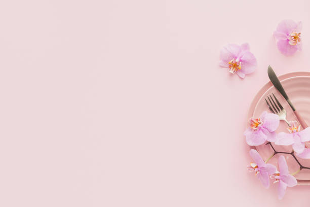 istock Flower and table settings overhead composition on light pink background. Pink ceramic plates, cutlery and perple orchid flowers. Holiday modern table decoration. Romantic date. 1282658325
