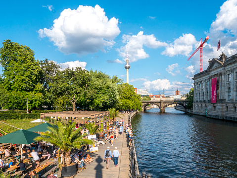 People relaxing, drinking and talking at beach bar next to the bode museum and spree river. The Berlin tv tower is visible on the horizon. The Spree river used to be the border between East and West Berlin.