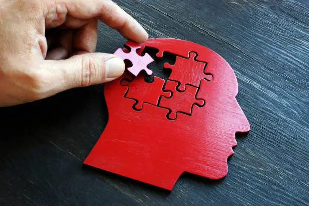 Treating mental illness and memory problems concept. The hand puts a piece of the puzzle on the shape of the head.
