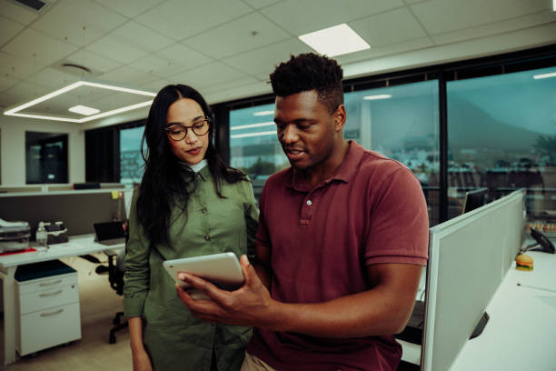 istock Multi-ethnic partners submitting business report using digital tablet standing in office block 1282662973