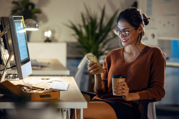 belle jeune femme d’affaires ayant le videocall avec le téléphone portable tout en travaillant avec l’ordinateur s’asseyant dans le bureau. - looking at camera smiling desk isolated photos et images de collection