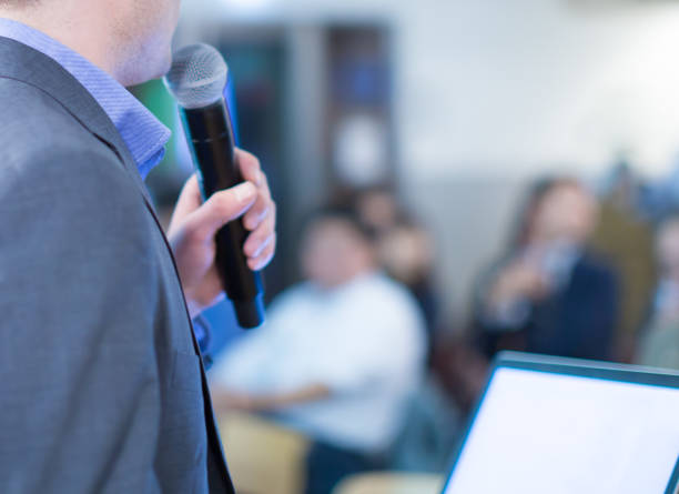 istock Conference photo audience and speaker giving speech. Seminar presenter on a panel during forum. Corporate manager in sales executive training discussion on stage. Investor pitch presentation. 1282666074