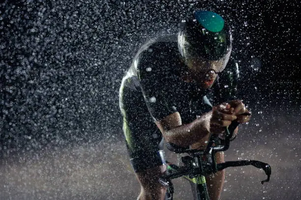 triathlon athlete riding professional racing bike fast  at night with bad weather and falling rain