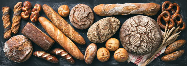 delizioso assortimento di pane appena sfornato su sfondo rustico scuro - baking baker bakery bread foto e immagini stock