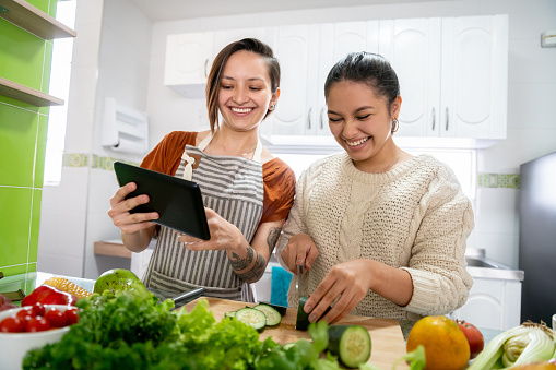 Couple of lesbians having fun cooking together at home and following a recipe on a tablet computer - LGBTQI lifestyle concepts