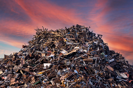 scrap metal heap at recycling junk yard against red sky at sunset