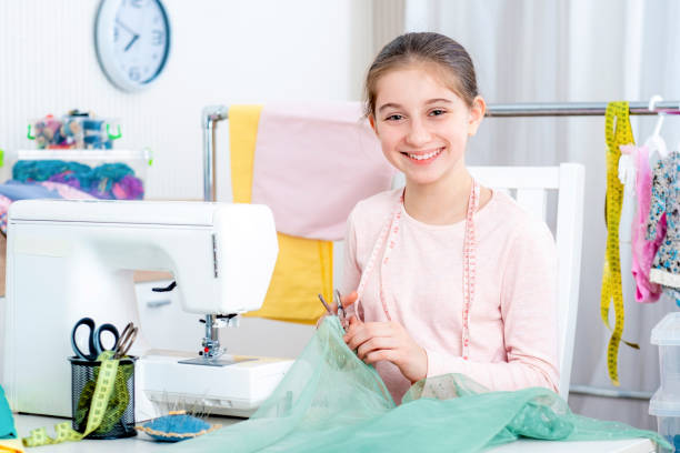 smiling little girl working at the sewing machine smiling little girl seamstress working at the sewing machine and smiling machine sewing white sewing item stock pictures, royalty-free photos & images