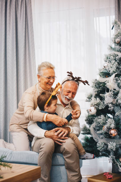 beau couple aîné tient leur petit-fils dans les genoux, embrassé, jouant. concept de noël. - senior couple grandparent cheerful happiness photos et images de collection