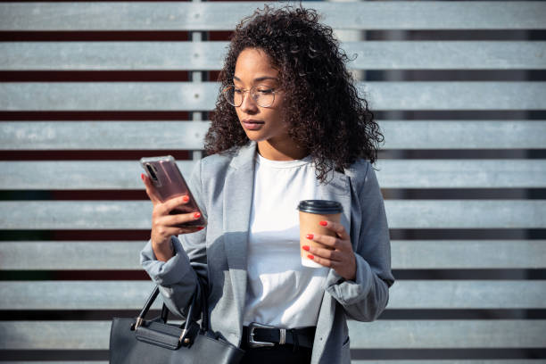 istock Confident young business woman using her mobile phone while drinking coffee standing in the street. 1282683920