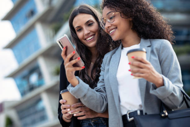 istock Two beautiful businesswomen using smart phone while drinking coffee walking around the city. 1282683947
