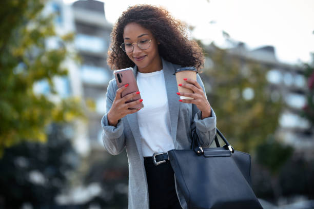 istock Pretty young business woman using her smart phone while drinking coffee walking down the street. 1282684513