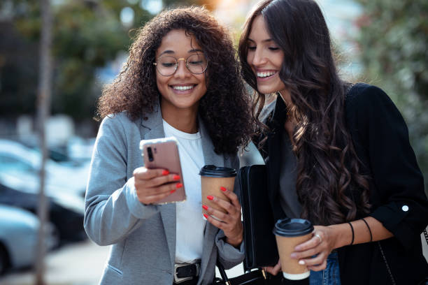 istock Two beautiful businesswomen using smart phone while drinking coffee walking around the city. 1282684537