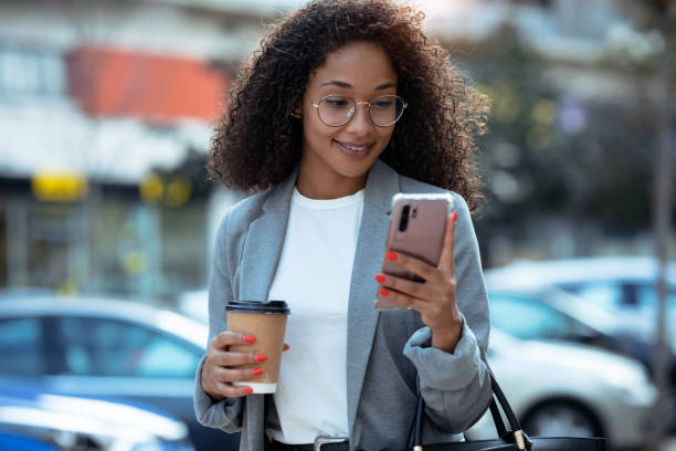 istock Pretty young business woman using her smart phone while drinking coffee walking down the street. 1282684565