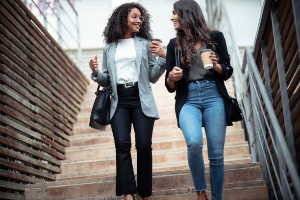istock Two beautiful businesswomen talking and drinking coffee while going down the stairs in the street. 1282684614