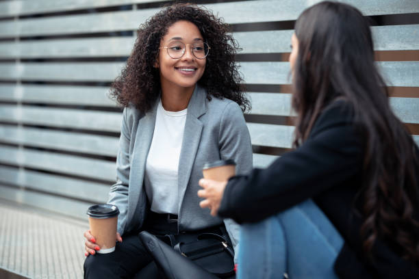 istock Two beautiful businesswomen talking while drinking coffee sitting on a bench on the street. 1282684939