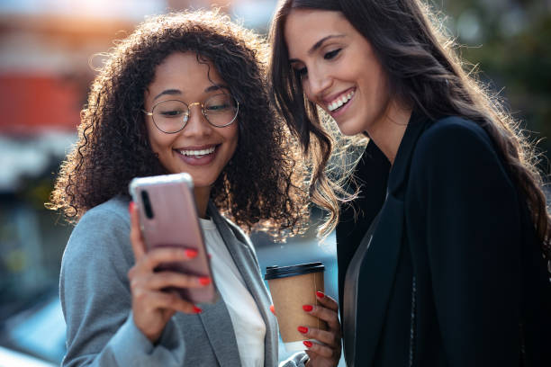 istock Two beautiful businesswomen using smart phone while drinking coffee walking around the city. 1282685027