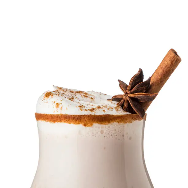 Glass of traditional Christmas eggnog cocktail decorated with cinnamon stick, grated nutmeg and anise star isolated on white background