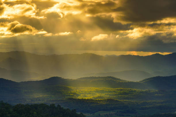 istock Yellow sun shafts through cloudy sky with long mountain range  and brighten foreest in Tak, Thailand 1282685978