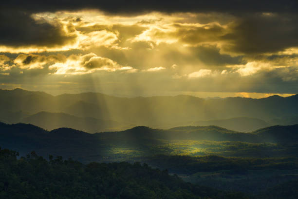 istock Yellow sun shafts through cloudy sky with long mountain range  and brighten foreest in Tak, Thailand 1282685980