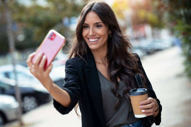 istock Smiling young business woman using her mobile phone while drinking coffee walking down the street. 1282686516