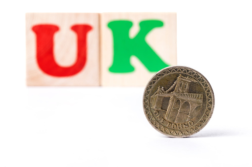 The abbreviation UK (United kingdom) folded from letters on children's cubes and a coin of one English pound on a white background