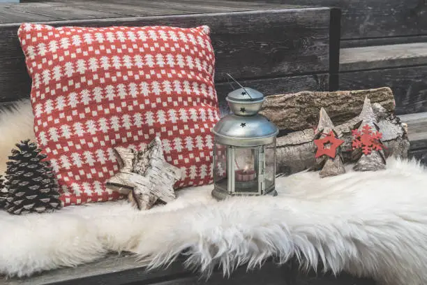 Wooden veranda with lambskin, red and white Christmas pillows, lantern and firewood