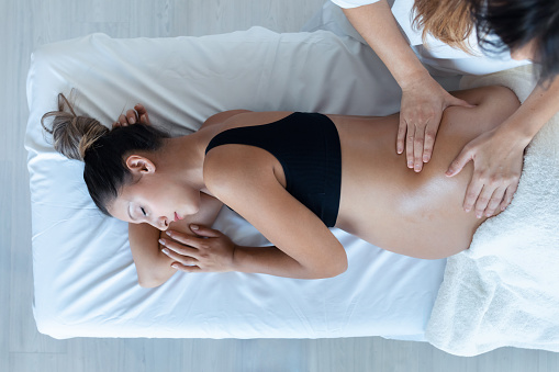 Hermosa mujer fisioterapeuta joven masajeando la barriga en la mujer embarazada en una camilla en casa. photo