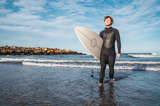 Portrait of young surfer leaving the water with surfboard under his arm. Sport and water sport concept.