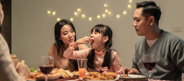 asian young little girl enjoy eating her meal crispy fried chicken together with family in christmas and new year party. the kid feeling happy to stay with parents and grandparents during holiday. - child party group of people little girls imagens e fotografias de stock