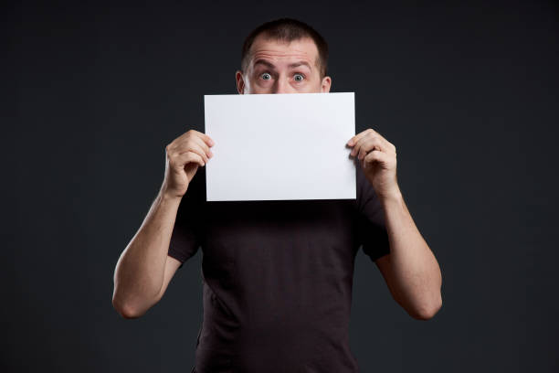 istock Man holds an empty poster paper sheet in his hands. Smile and joy, place for text, copy space 1282700586